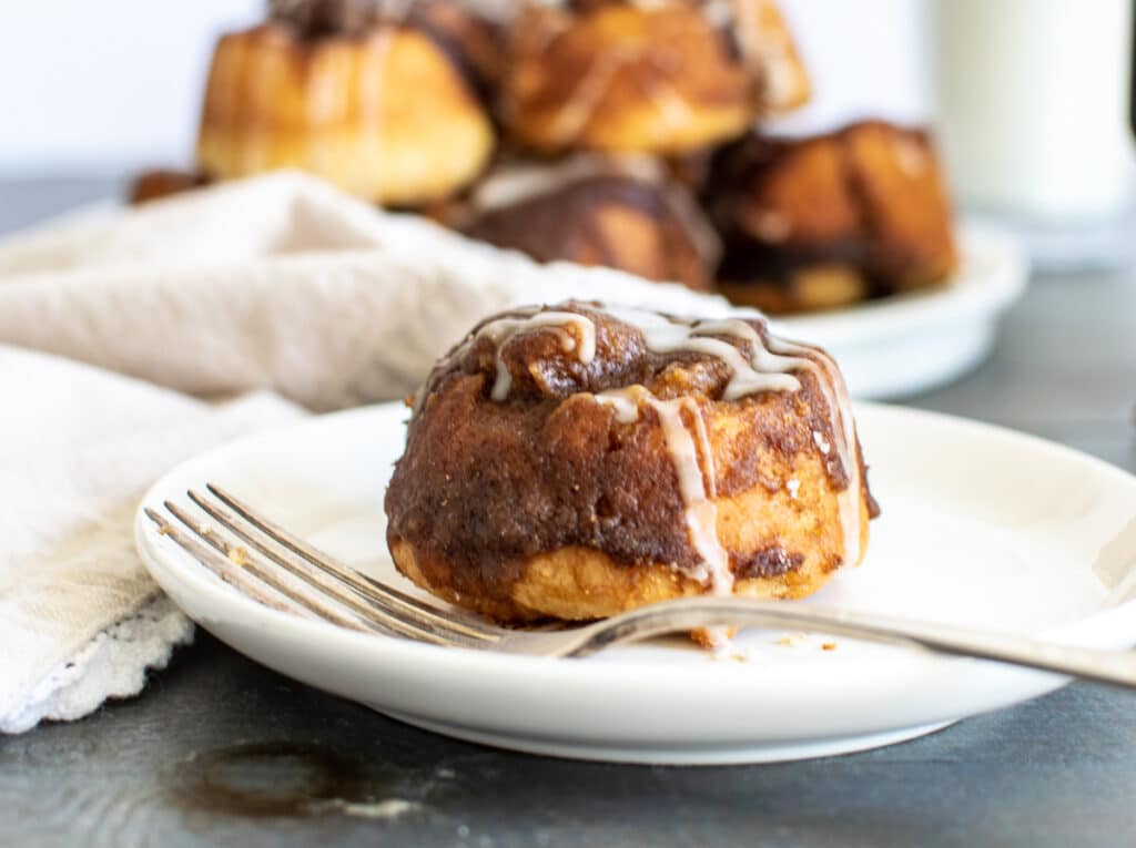 Cinnamon rolls without egg or yeast with a simple glaze on a white plate and silver fork.